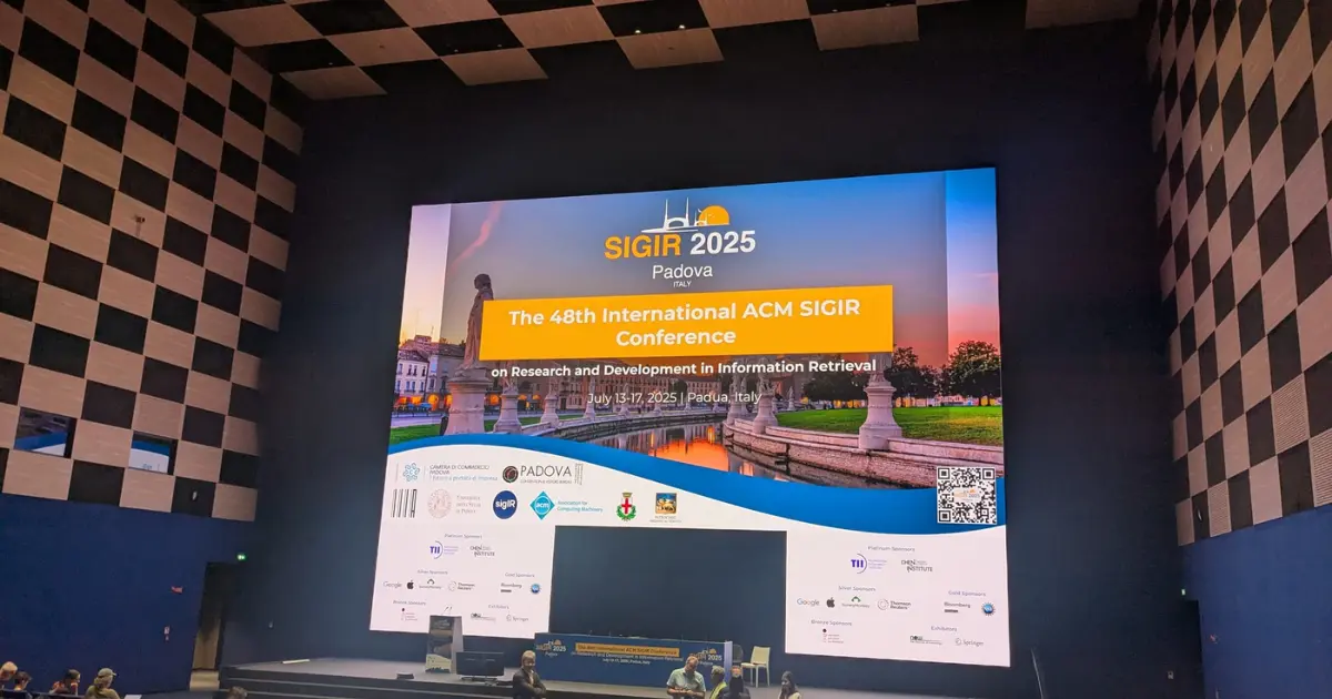 Conference scene in a large auditorium with a "SIGIR 2025" banner on the projected screen, a speaker on stage, and attendees 